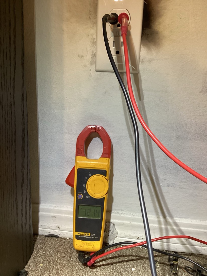 Clamp meter with probes connected to electrical outlet for testing.