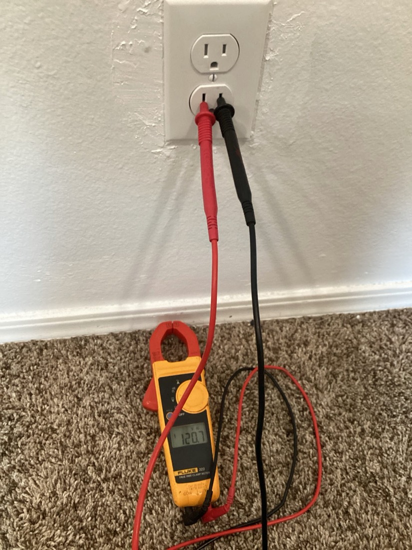 Clamp meter testing electrical outlet with red and black leads.