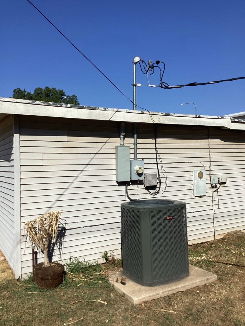 AC condenser unit showing electrical panel, conduit, and service connections on side of home.