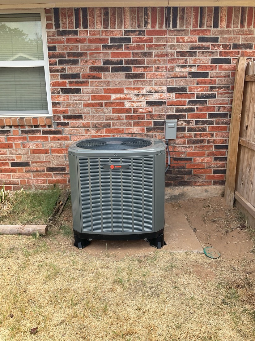 Gray AC unit installed against brick wall with wooden fence.