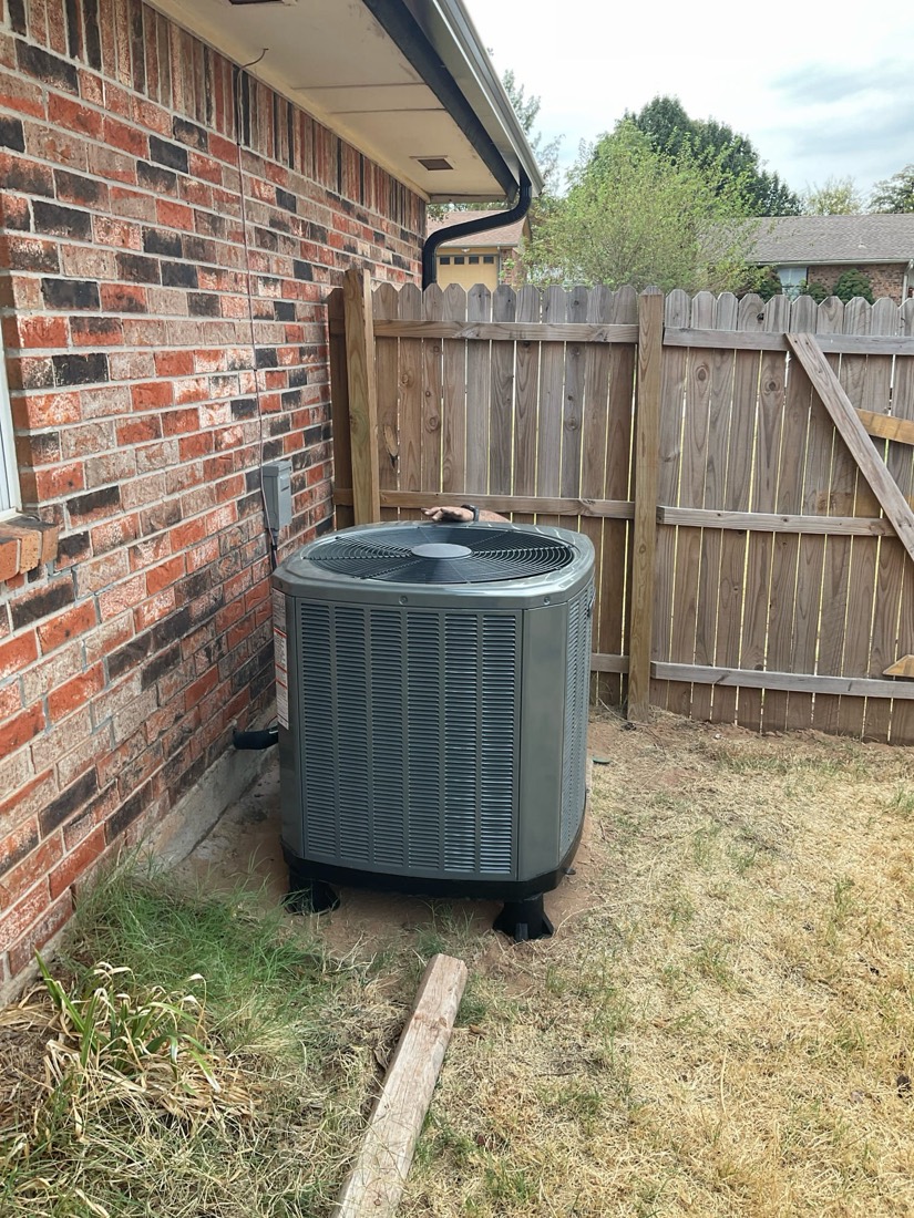 Gray AC condenser unit installed against brick home exterior.
