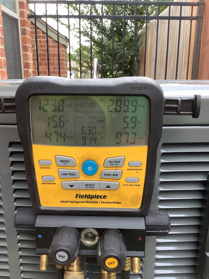 Yellow and black Fieldpiece refrigerant manifold gauge connected to AC condenser with brass fittings.