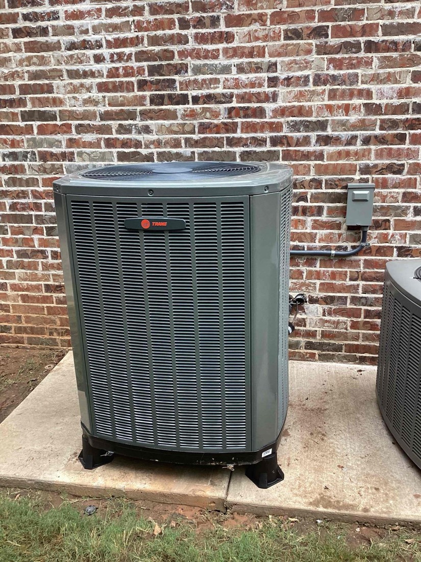 Trane outdoor AC condenser unit on concrete pad against brick