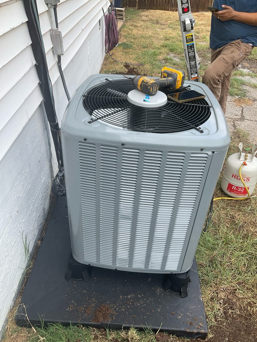Gray AC condenser unit with tools on top.